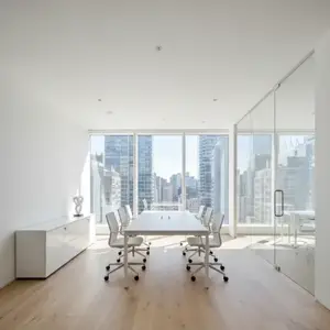 Minimalist modern office interior with a clean white meeting table and chairs against a bright city skyscraper background.